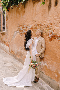 意大利威尼斯婚礼 新娘和新郎走在城市空无一人的街道上 新婚夫妇站在附近 在一栋漂亮房子的橙色墙壁附近拥抱风格夫妻套装裙子幸福异性图片