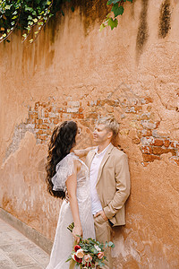 意大利威尼斯婚礼 新娘和新郎走在城市空无一人的街道上 新婚夫妇站在附近 在一栋漂亮房子的橙色墙壁附近拥抱奢华夫妻目的地天井玫瑰花图片