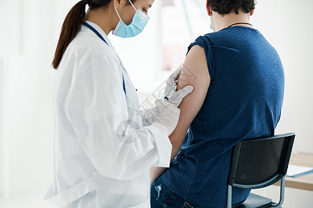 以医疗面具向男子注射蓝色T恤袖子接种疫苗的女医生图片