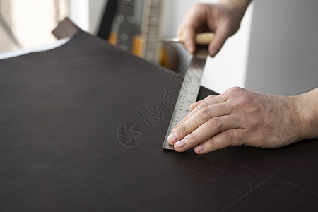 男人的手拿着锥子和金属尺子 在他的车间里做皮钱包 与棕色天然皮革的工作过程 工匠拿着制作工具 在皮革上做标记图片