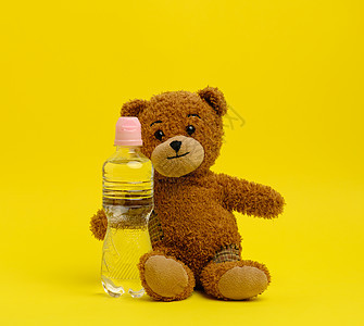 小泰迪熊在黄色背景上 拿着透明水瓶的小泰迪熊图片