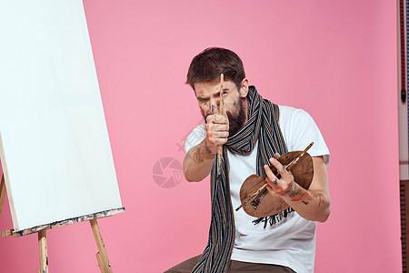男性艺术家用围巾围着他的脖子涂料画画粉红色的艺术背景成人画笔创造力职业艺术品画家工作刷子画架白色图片
