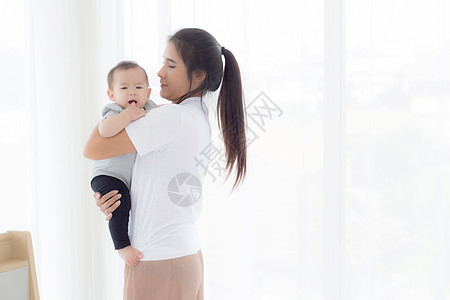 年轻的亚洲母亲抱着小女婴在家里的卧室里一起散步 妈妈带着女儿和照顾 父母和孩子的关系 蹒跚学步的孩子和父母 室内 家庭观念女性拥图片
