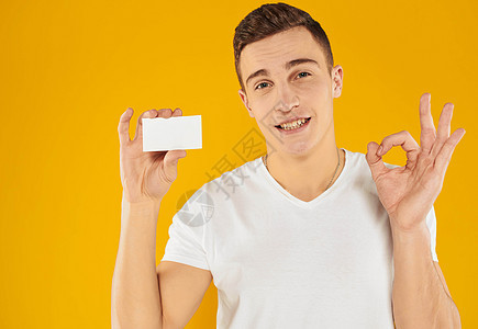 一个穿白色T恤衫的男人 在黄色背景的作物风景上 展示了一张信用卡人士广告牌微笑管理人员工人广告横幅标语工作商业图片