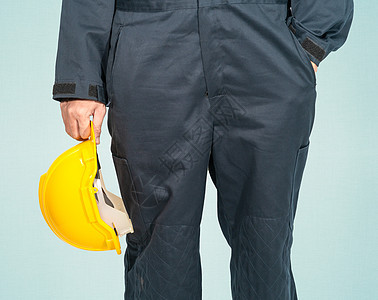 站在蓝色覆盖层的工人 拿着黄色硬头巾安全帽工作室头盔塑料制服建筑师手臂制造业男性帽子图片