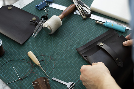 男士手在他的工作室里制作皮革钱包 与棕色天然皮革的工作过程 拿着制作工具的工匠配饰剪刀皮艺缝纫皮肤机器裁缝商业职业手工图片