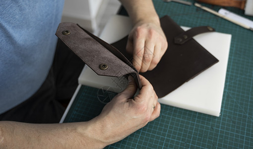 男士手在他的工作室里制作皮革钱包 与棕色天然皮革的工作过程 拿着制作工具的工匠工艺品店铺皮匠产品职业锥子桌子商业作坊前锋图片