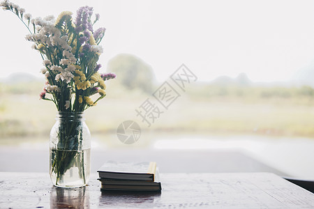 玻璃花瓶中的花花束和窗口旁边的书植物群花朵风格桌子装饰窗户瓶子图片