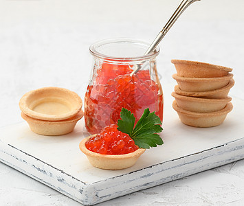 白桌上一个玻璃罐和圆小桶中的红色鱼子酱食物玻璃密友美味午餐桌子熟食橙子奢华鱼子图片