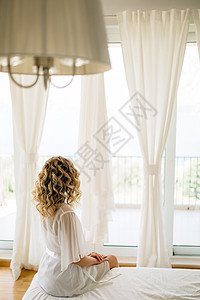 坐在宽阔的阳台窗户边 有白色窗帘的床边的一位穿着温柔皮质的新娘图片