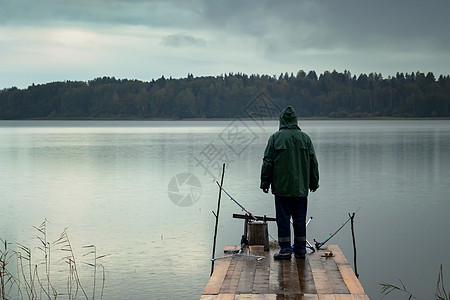 雨天独自一人捕鱼 站在木桥上 在钓鱼杆上钓鱼图片