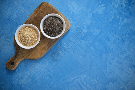 藜麦和奇亚籽是健康饮食的有机食品 在一个圆碗里 两个白色杯子 蓝色纹理是用蓝色油画颜料绘制的宏观木头烹饪食物收藏营养排毒谷物稀饭图片