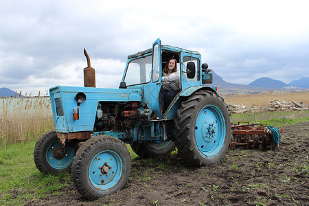 拖拉机上的女孩在田里 秋天把拖拉机的地耕种 农业工作收成轮子蓝色青年装备空气农作物土地越野运输图片