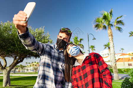 由于大肠病毒的流行 身穿格子衬衫的年轻学生夫妇戴着防护面具自拍 年轻的白人男子与亲切地靠在他肩上的女友合影图片