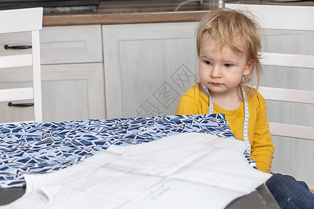 可爱的小男孩坐在一张桌子旁 桌上放着准备回家缝纫的布料图片