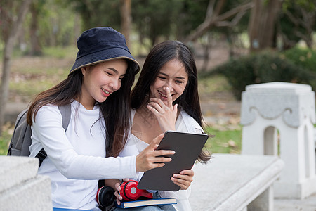 Asin女学生穿着便衣坐在户外 深思熟虑地看书 可爱的女生向朋友解释一些东西 她的朋友指出图片