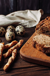 将无黑酵母荞麦面包切成一块 放在一块切碎的木板上 旁边是鹌鹑蛋和意大利格里西尼 放在亚麻桌布上 放在一张乡村风格的木桌上 早餐烹图片