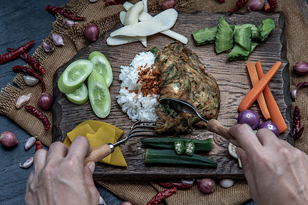 泰国当地的美食风格 手用勺子在茉莉花米饭上舀油炸金合欢煎蛋卷或 chaom 鸡蛋 配料和木制背景上的新鲜蔬菜营养午餐草本植物噼啪图片