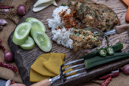 泰国当地的美食风格 手用勺子在茉莉花米饭上舀油炸金合欢煎蛋卷或 chaom 鸡蛋 配料和木制背景上的新鲜蔬菜午餐辣椒噼啪盘子营养图片