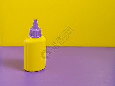 带紫色盖帽的黄色瓶子站在带黄色背景的紫色桌子上图片