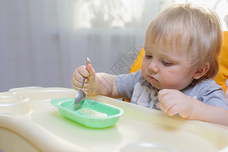 小孩坐在高椅子上 用勺子吃饭厨房童年午餐婴儿微笑男生教育食物快乐盘子图片