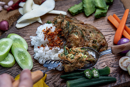 泰国当地的美食风格 手用勺子在茉莉花米饭上舀油炸金合欢煎蛋卷或 chaom 鸡蛋 配料和木制背景上的新鲜蔬菜草本植物食物黄瓜油炸图片