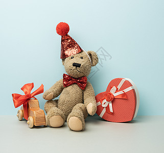 红帽子的棕色泰迪熊坐在蓝色背景上红色娃娃庆典帽子童年喜悦展示孩子们礼物动物图片