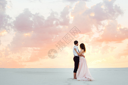一对年轻夫妇 一个穿黑裤子的男人和一个穿粉红色裙子的女孩 沿着白沙走来衬衫乐趣树木沙漠沙滩脚印白色夫妻自由跑步图片