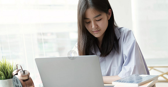 亚洲美丽的女学生在家中用笔记本电脑学习图片