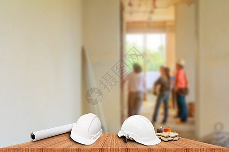 两个白色安全帽和皮手套卷尺 卷纸计划蓝图 用于工程工作内部建筑工地建筑在木地板桌上 复制空间添加文本 模糊背景安全水泥桌子工程师图片