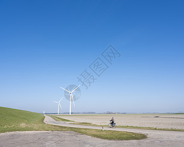 在泽兰杜切省丘顿杜伊沃土地农村景观中骑自行车和风力涡轮机的男子图片