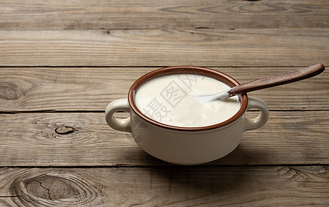 棕色陶瓷碗中的酸奶油和桌上的木勺子鞭打牛奶酸奶营养奶制品桌子产品盘子白色食物图片
