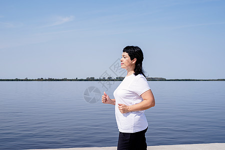 在河边附近慢跑的活跃老年女子成人运动女性享受力量活动退休训练运动装跑步图片