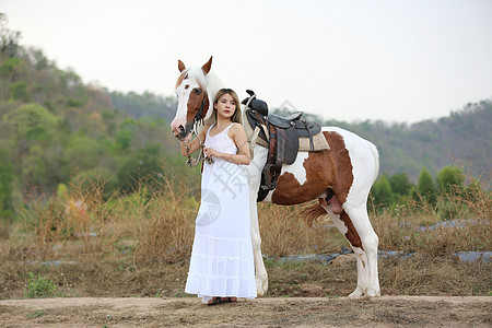 穿着裙子的女性在日落时 在田地风景中骑马对抗天空农村动物女孩骑士女士荒野爱好场地闲暇草地图片