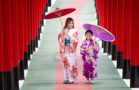 和服中的妇女和小女孩拿着伞走进来 在圣殿红门 在日本花园的红色门女性地标宗教旅游女孩文化戏服隧道裙子建筑学图片