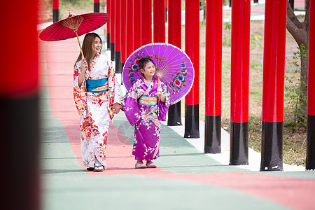 和服中的妇女和小女孩拿着伞走进来 在圣殿红门 在日本花园的红色门隧道人行道戏服传统女性神道女士旅行小路裙子图片