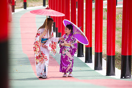 和服中的妇女和小女孩拿着伞走进来 在圣殿红门 在日本花园的红色门宗教戏服建筑学文化神道女孩人行道神社隧道传统图片