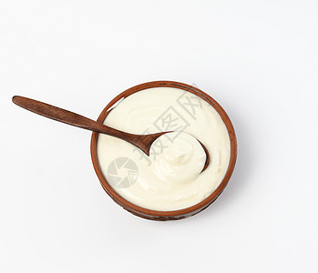 棕色陶瓷碗中的酸奶油和白背景的木勺子图片