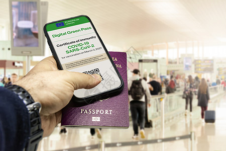 男手拿着手机 屏幕上有欧盟疫苗接种证书 机场内有传统护照卫生限制保健授权联盟旅行安全飞机场代码认证图片