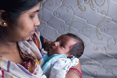 特写一个可爱的新生男婴的脸 高兴地看着坐在妈妈膝上的妈妈 一个月大 可爱的小婴儿蹒跚学步 印度种族 正视图 母亲节快乐背景图像儿图片
