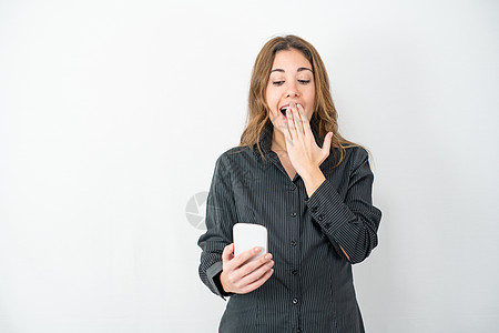 工作室拍摄的年轻模特女性穿着灰色衬衫商务服装 与白色复制空间背景隔离 惊讶地看着智能手机 手放在嘴上 新技术的概念图片