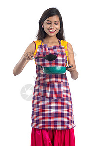 以白色背景持有厨房用的年轻印度妇女SPO STPULA 拖拉机和锅等食物烹饪手势衣服围裙金属勺子平底锅肩胛骨餐具图片