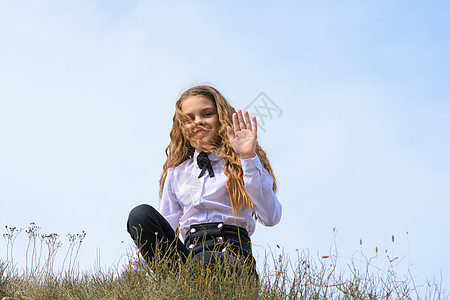 一个身穿白衬衫 打领结的女孩坐在天空背景下田野的地上 挥舞着笔到画框图片