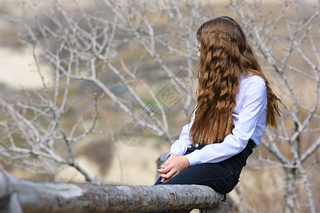 女孩坐在木栅栏上 望着远处的距离图片