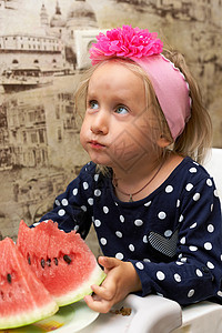 一个女孩坐在桌子上 拿着一块红西瓜 抬头望着图片