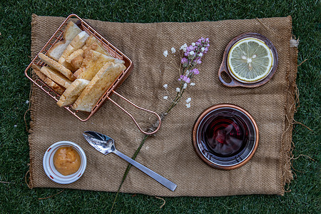 茶叶和柠檬在公园绿草坪上 与焦糖加酸土豆一起享用小吃面包甜点草地麻布早餐食物享受木头饮料图片