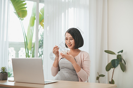 美丽的孕妇吃着快乐的酸奶母亲腹部女性肚子生活成人笔记本母性婴儿电脑图片