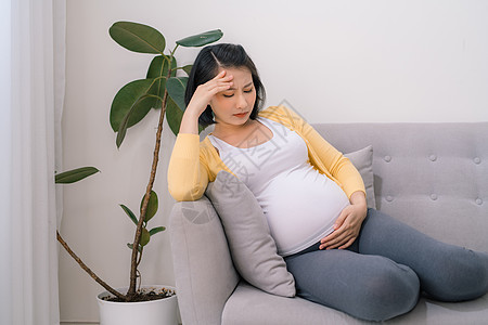 孕妇在家里起居室收缩 怀孕妇女在家客厅收缩说谎头痛枕头母亲女性沙发成人腹部休息母性图片