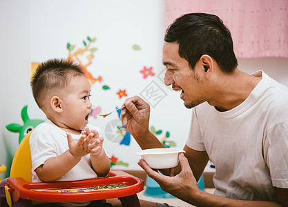 做爸爸的妈妈在喂他儿子一岁小孩 坐在椅子上图片