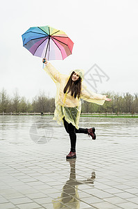 美丽的黑发美女 在雨中拿着多彩的雨伞雨衣喜悦女性下雨街道季节微笑彩虹城市快乐图片